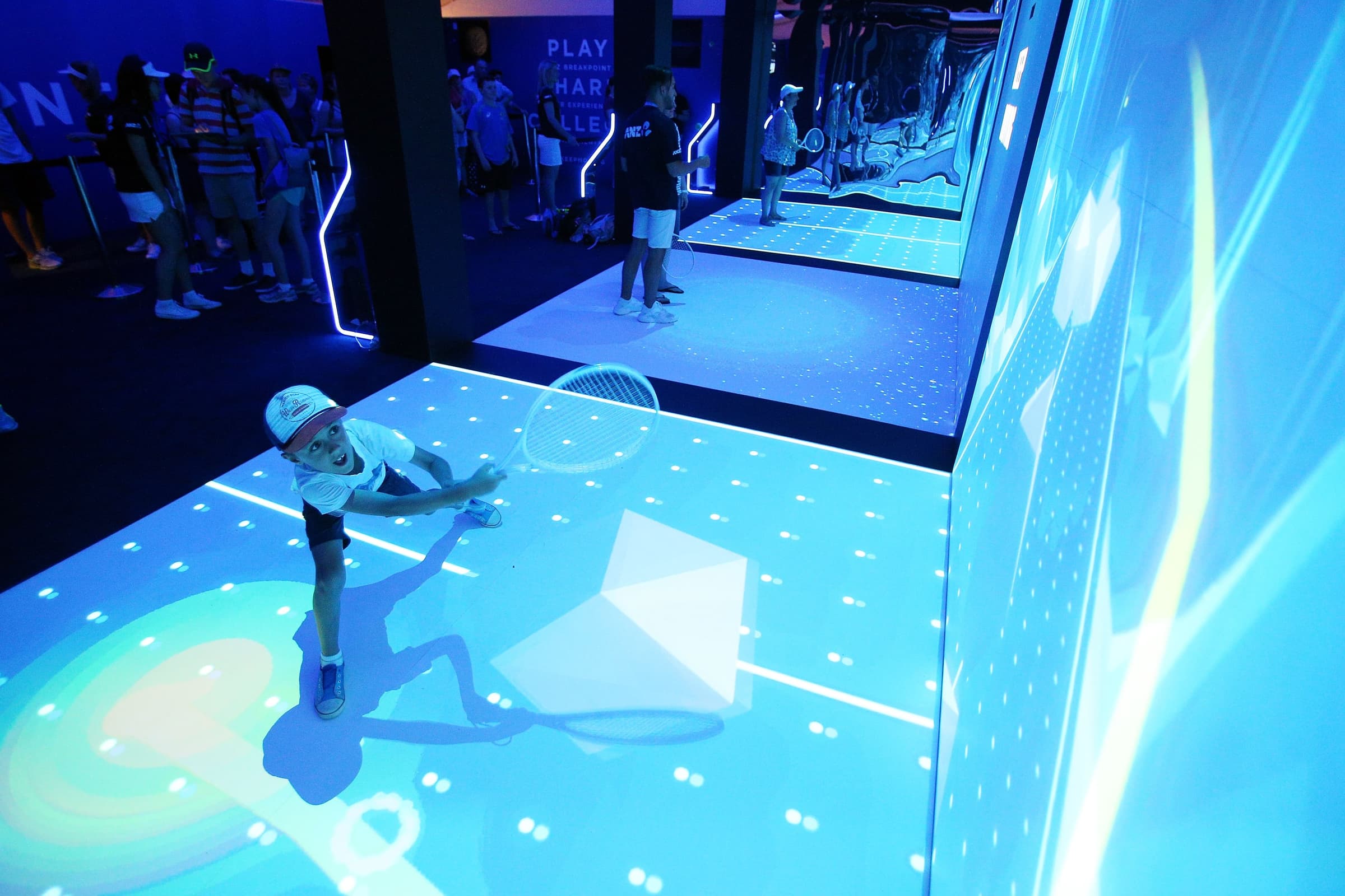 A young participant swinging a tennis racket inside the projected ANZ Breakpoint court.