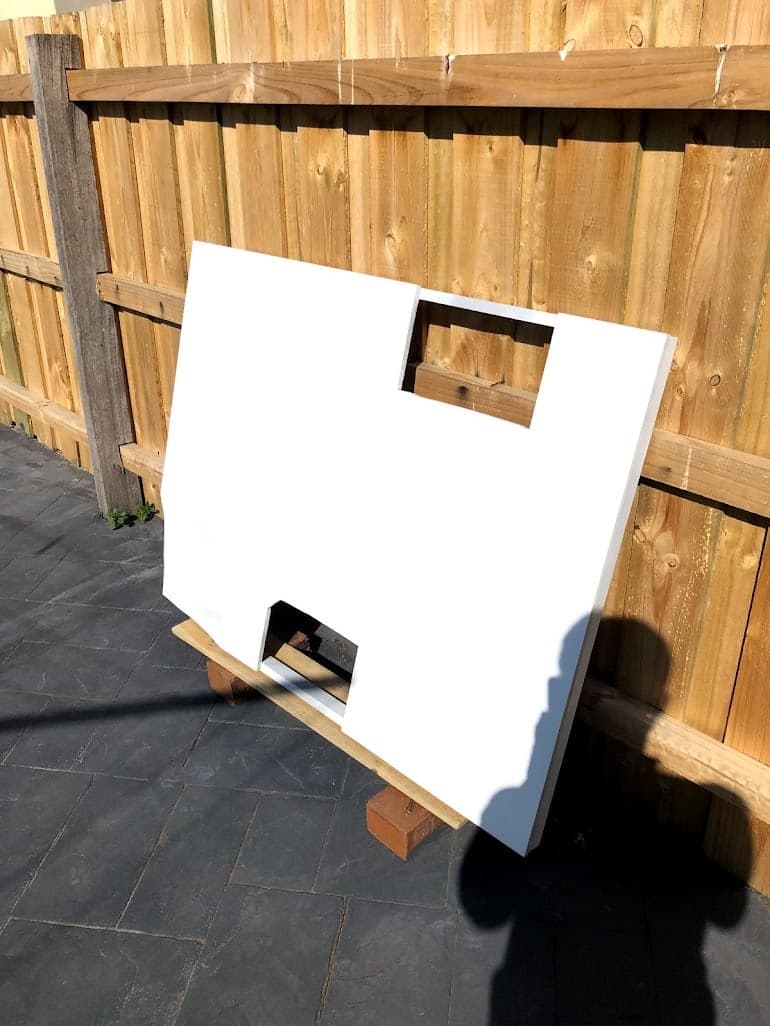 A fabricated white panel for the H2.0 installation drying against a timber fence in a backyard.