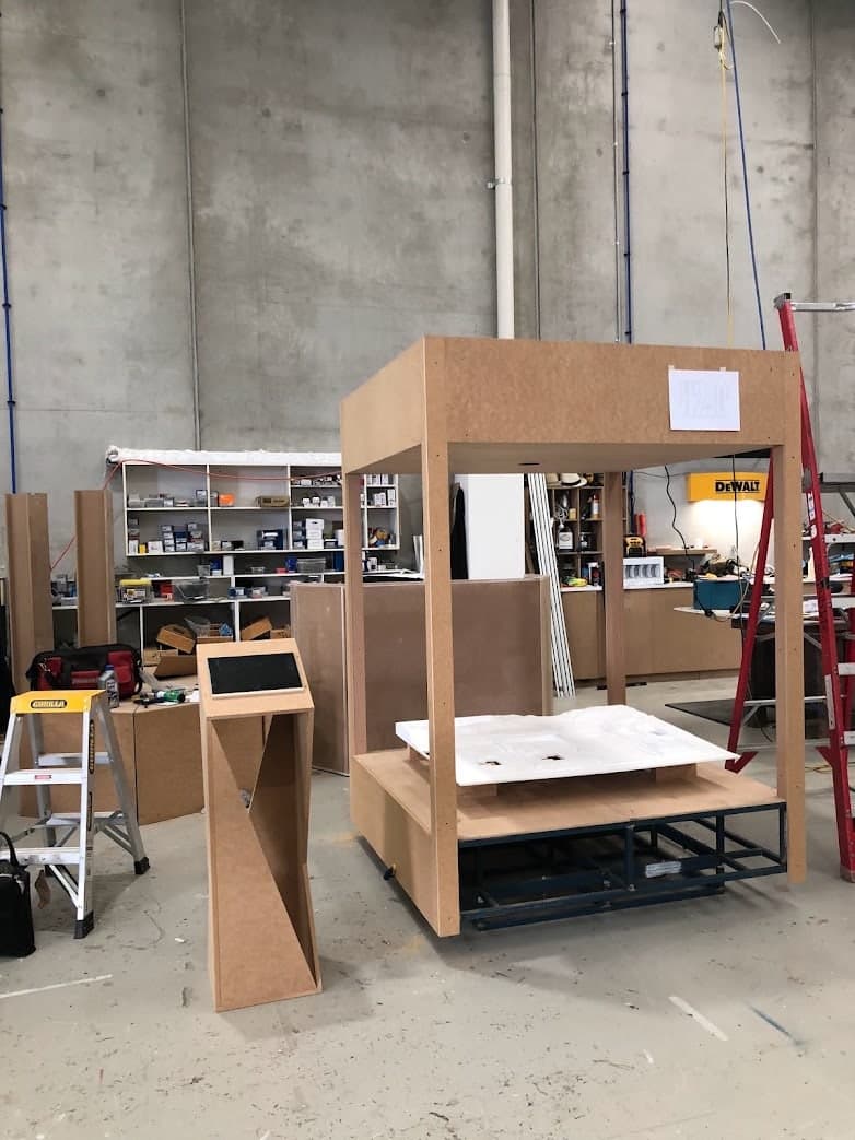 Workshop view of the CNC-cut H2.0 model inside the unfinished full-height stand, with its separate touchscreen pedestal.