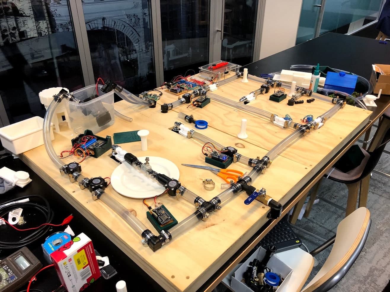 The exposed H2.0 water loop under assembly, with clear pipes, valves, sensors and printed parts arranged on a timber base.