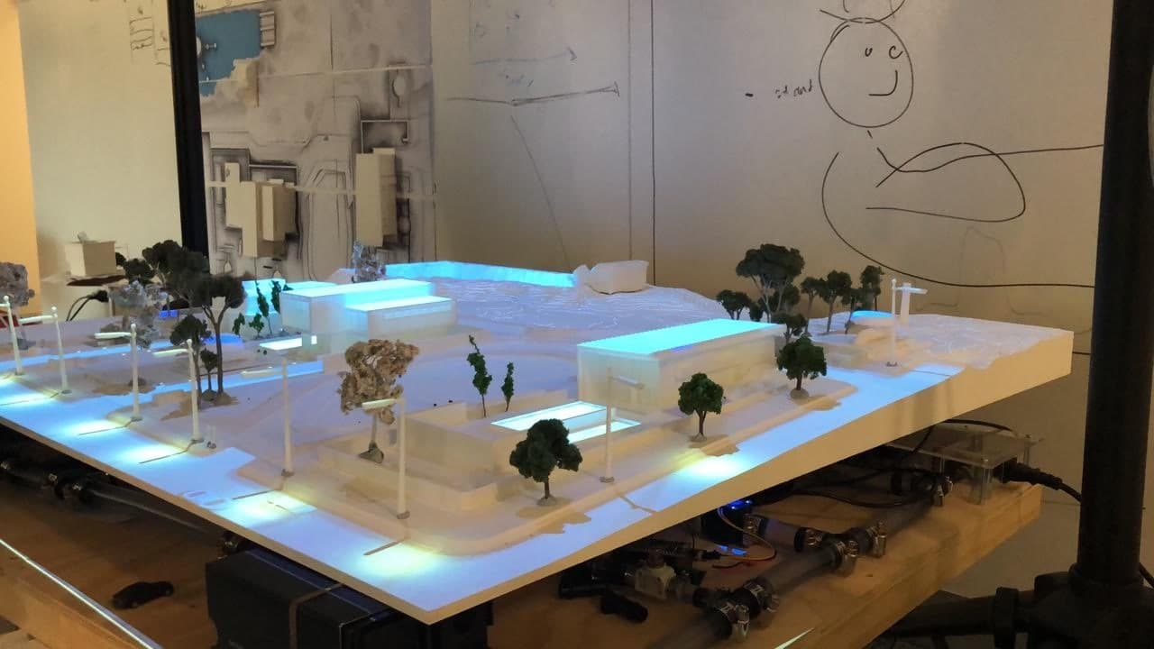 The CNC-cut H2.0 surface fitted above the working water system, with buildings, trees, lights and projected water paths under test.