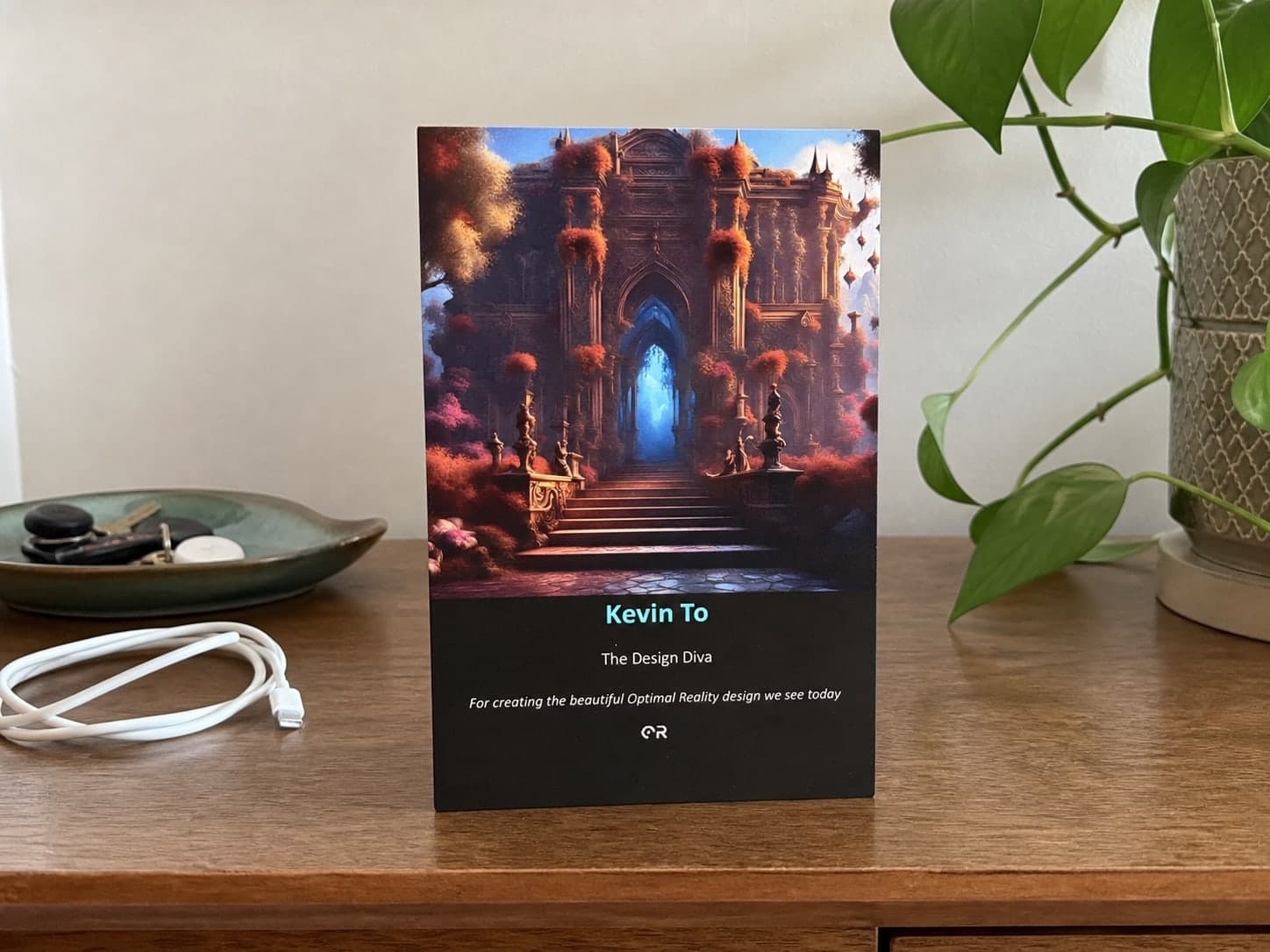 The Optimal Reality team keepsake presented to Kevin To, standing on a timber sideboard beside a plant, keys and a charging cable.
